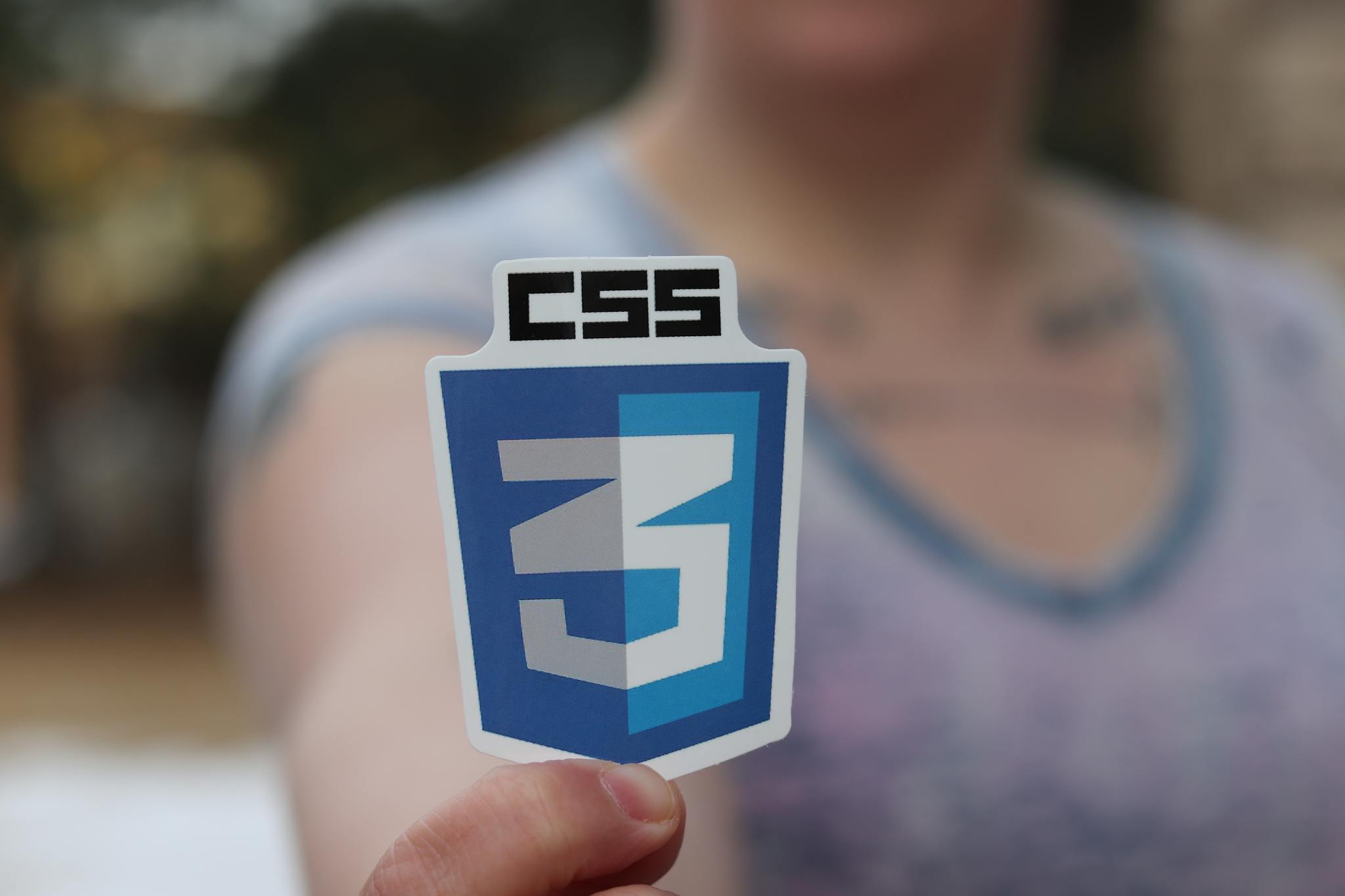 Close-up photograph of a CSS3 logo sticker held by a person with blurred background.